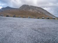 a group of cars that are parked in front of a mountain peak, with a few tent and buildings on the side of the hill