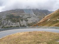 a curved road winds through mountains with low clouding in the distance during daytime hours