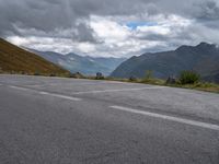 the road is empty and the clouds are coming in on the mountains behind it,