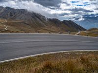 a curved road near many mountains on a cloudy day with clouds in the sky and people walking on the sidewalks