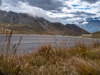 a curved road near many mountains on a cloudy day with clouds in the sky and people walking on the sidewalks