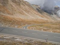 a motorcycle on a winding road with mountains in the background, and a plume of smoke behind the road