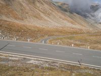 a motorcycle on a winding road with mountains in the background, and a plume of smoke behind the road