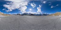 a 360 - shot of an asphalt road with a sky background and snow capped mountains in the distance