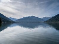 the boat sits in the middle of the calm water and mountains surrounding it are covered with snow capped peaks