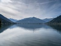 the boat sits in the middle of the calm water and mountains surrounding it are covered with snow capped peaks