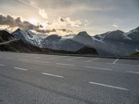 a car is parked along the mountain side near a parking area under some snow covered mountains