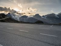 a car is parked along the mountain side near a parking area under some snow covered mountains