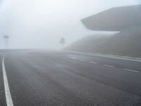 the empty street has a few traffic signs and a foggy background on it,