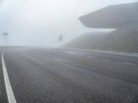 the empty street has a few traffic signs and a foggy background on it,