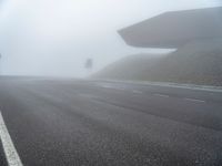 the empty street has a few traffic signs and a foggy background on it,