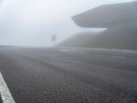 the empty street has a few traffic signs and a foggy background on it,