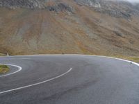 a motorcyclist is riding the curve of an empty road in front of the mountains