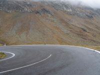 a motorcyclist is riding the curve of an empty road in front of the mountains