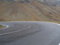 a motorcyclist is riding the curve of an empty road in front of the mountains