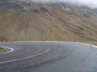 a motorcyclist is riding the curve of an empty road in front of the mountains