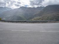 a person riding on a motorcycle down a highway under a cloudy sky and mountains with a road going up