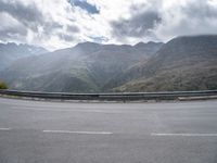 a person riding on a motorcycle down a highway under a cloudy sky and mountains with a road going up