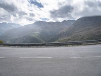 a person riding on a motorcycle down a highway under a cloudy sky and mountains with a road going up