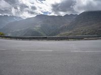 a person riding on a motorcycle down a highway under a cloudy sky and mountains with a road going up