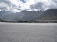 a person riding on a motorcycle down a highway under a cloudy sky and mountains with a road going up