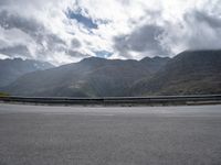 a person riding on a motorcycle down a highway under a cloudy sky and mountains with a road going up