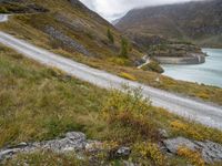 a person on a bike riding down the road beside a lake in a mountainous area