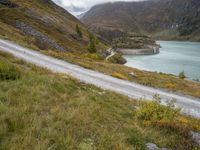 a person on a bike riding down the road beside a lake in a mountainous area