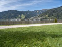 a view of the mountain, a lake and a wooden fence around a bench sitting on grass by the water