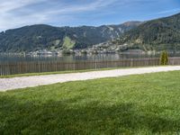 a view of the mountain, a lake and a wooden fence around a bench sitting on grass by the water