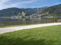 a view of the mountain, a lake and a wooden fence around a bench sitting on grass by the water