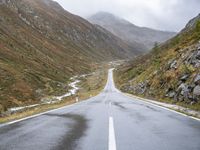 a wet road winds through the mountains to the right of the camera with a stop sign beside it