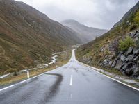 a wet road winds through the mountains to the right of the camera with a stop sign beside it