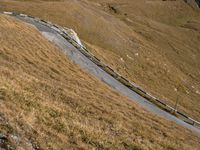 a steep winding road winds up into the mountains of scotland, which is covered with brown grass