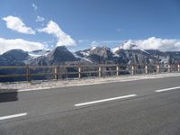 a van with snow - capped mountains in the background on a road side with railing