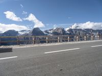 a van with snow - capped mountains in the background on a road side with railing