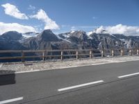 a van with snow - capped mountains in the background on a road side with railing