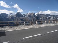 a van with snow - capped mountains in the background on a road side with railing