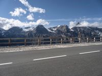 a van with snow - capped mountains in the background on a road side with railing