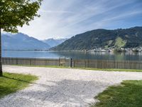 a park bench near the water and some mountains in the background and some grass and trees