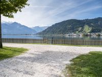 a park bench near the water and some mountains in the background and some grass and trees