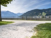 a park bench near the water and some mountains in the background and some grass and trees