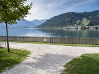 a park bench near the water and some mountains in the background and some grass and trees