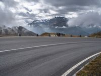 a paved road with mountains behind it under a cloudy sky and clouds above it at the top of a mountain range