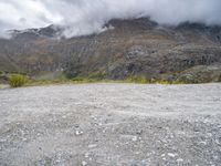 a mountain side with some very large mountains near a river and clouds above it, and a sign that says don't stop there