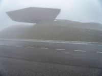 a building surrounded by a mountain of rubble on top of a highway in the fog