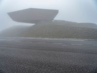 a building surrounded by a mountain of rubble on top of a highway in the fog