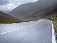 a lone road stretches through a wide valley with hills in the background below and some clouds above it