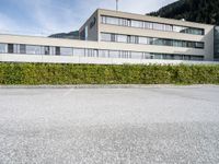 an office building with windows and shrubbery lining the sides of the street outside of it