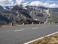 a motorcycle driving on a road between two mountains with a snow covered mountain in the distance